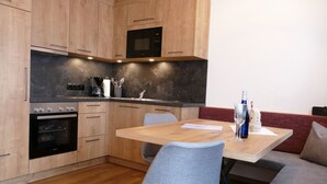 A modern kitchen with wooden cabinets, a built-in oven, a microwave, and a dining area with a table and chairs. - Contemporary Apartment in Gerlosberg Near Forest (Gerlosberg)