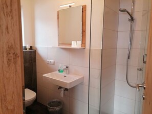 Ein Badezimmer mit einem weißen Waschbecken, einem Spiegel, einer Dusche und einer Toilette.