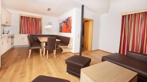 A modern living room with a dining area, a kitchen, and a wooden door leading to another room. - Apartment in Wald im Pinzgau Near Ski Slope (Wald im Pinzgau)