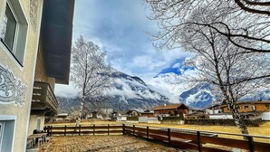 Une cour avec un sol en briques, une clôture en bois et une vue sur des montagnes enneigées.