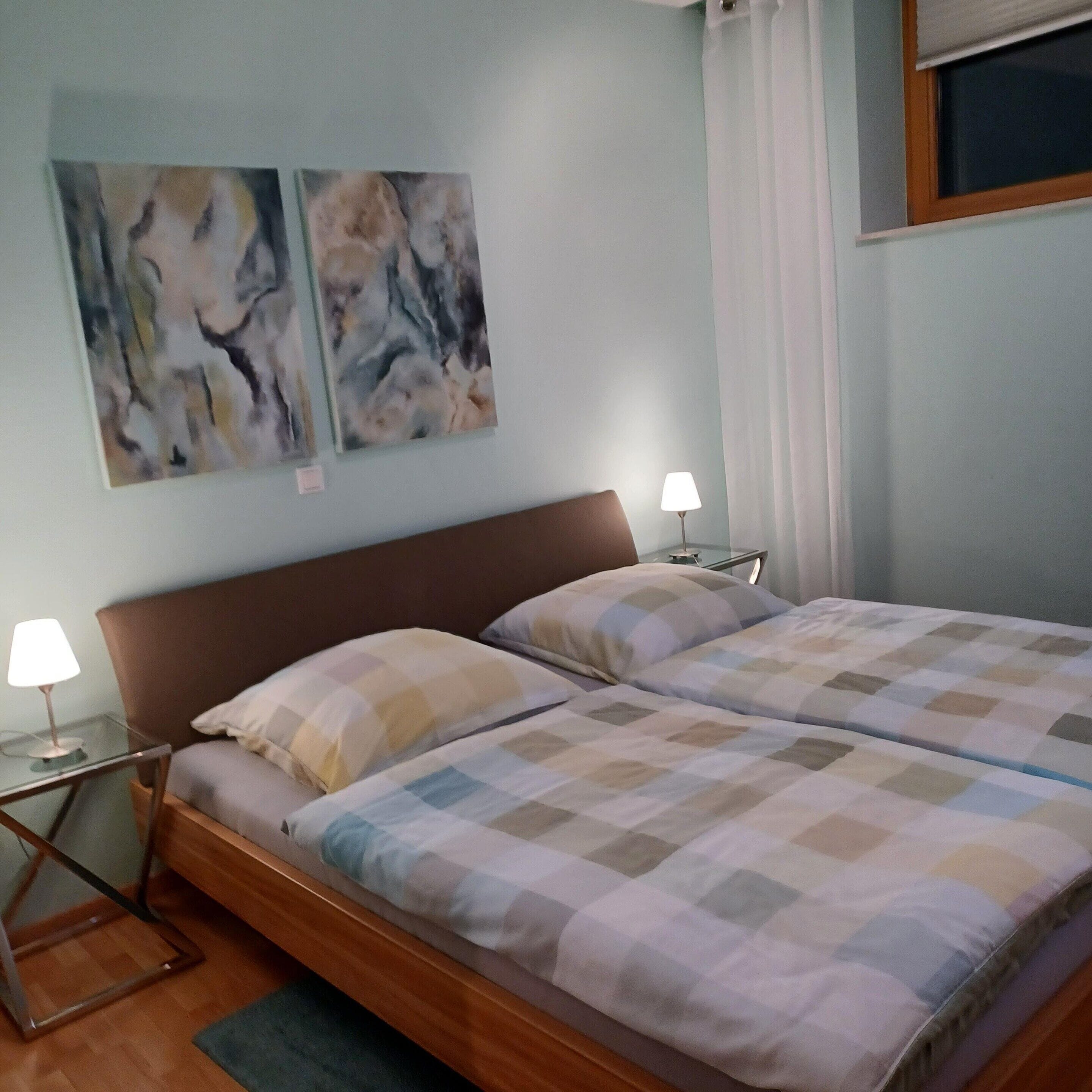 Un lit double avec une tête de lit en bois, deux lampes de chevet et une couvre-lit à carreaux.