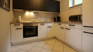 Cozinha com armários brancos, fogão, forno, micro-ondas e janela com vista para o verde.