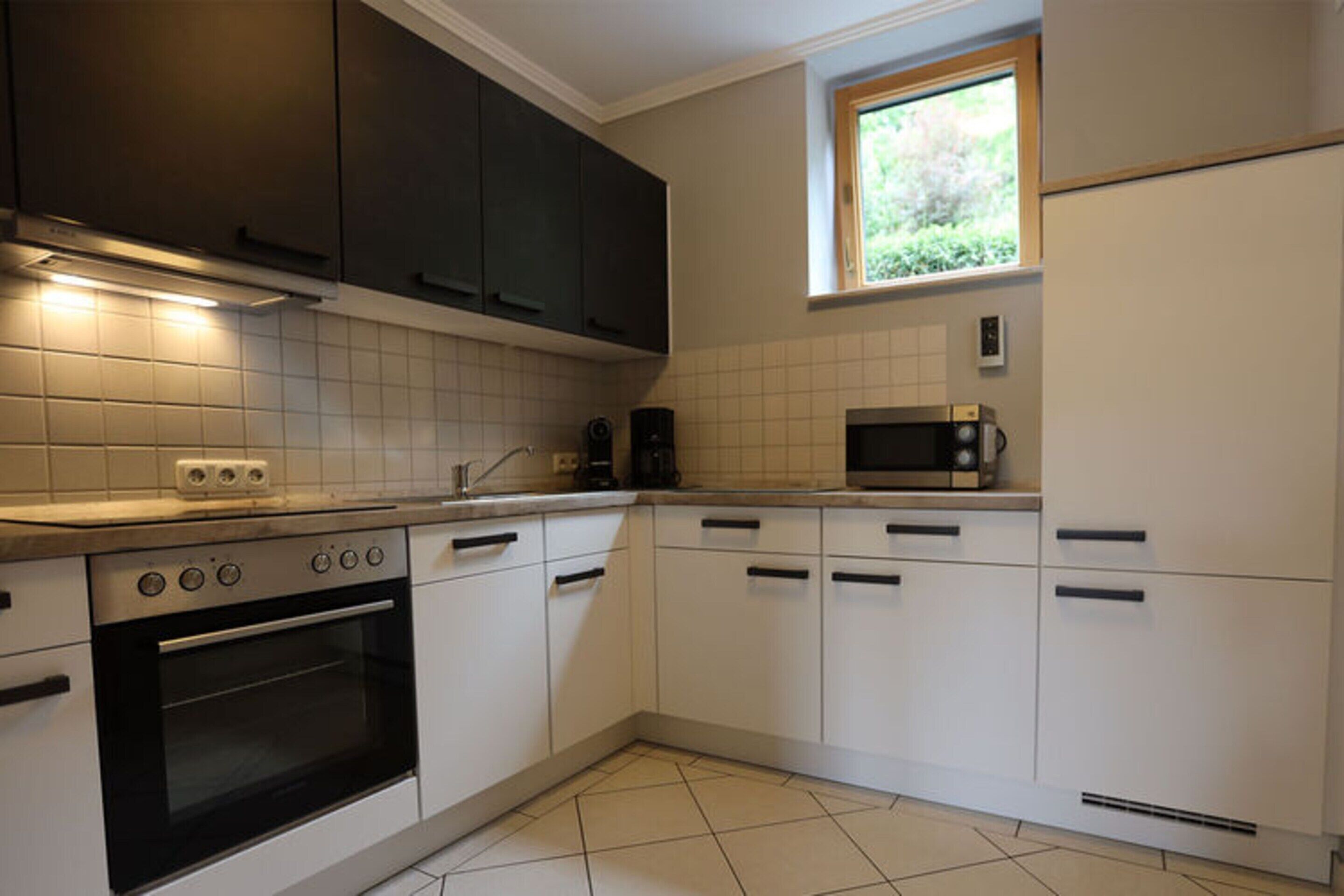 Una cucina con mobili bianchi, un fornello, un forno a microonde e una finestra sopra il lavello.