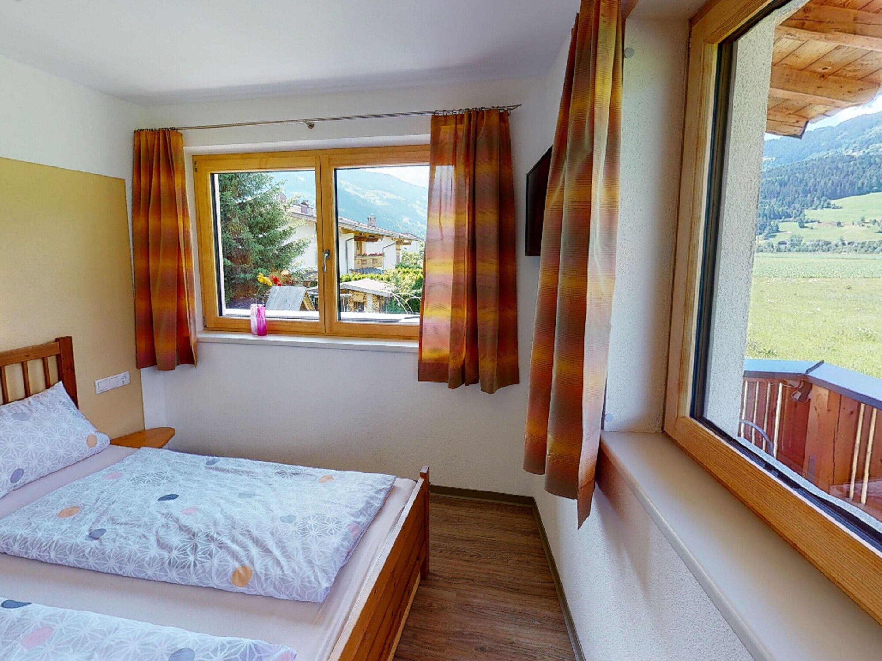 A bedroom with a bed, a window with curtains, and a view of a mountainous landscape.
