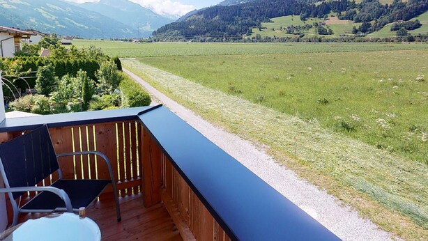 A balcony with a wooden floor, a metal chair, and a table. It overlooks a green field and mountains in the distance. - Idyllic Apartment in Stumm With Panoramic View (Stumm)