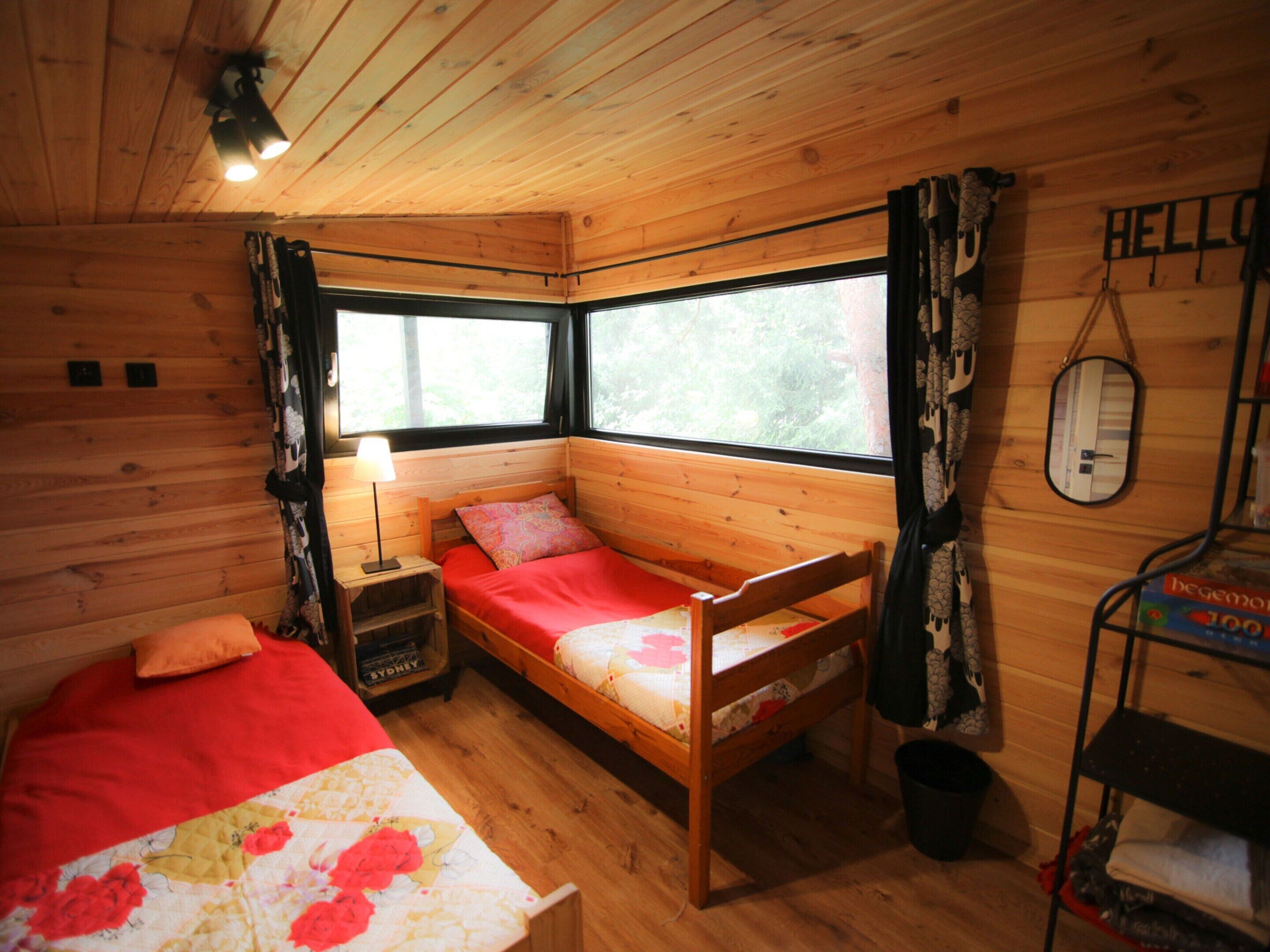 Acogedora habitación de cabaña con cama de madera, mesita de noche, lámpara y ventana con vistas a árboles.