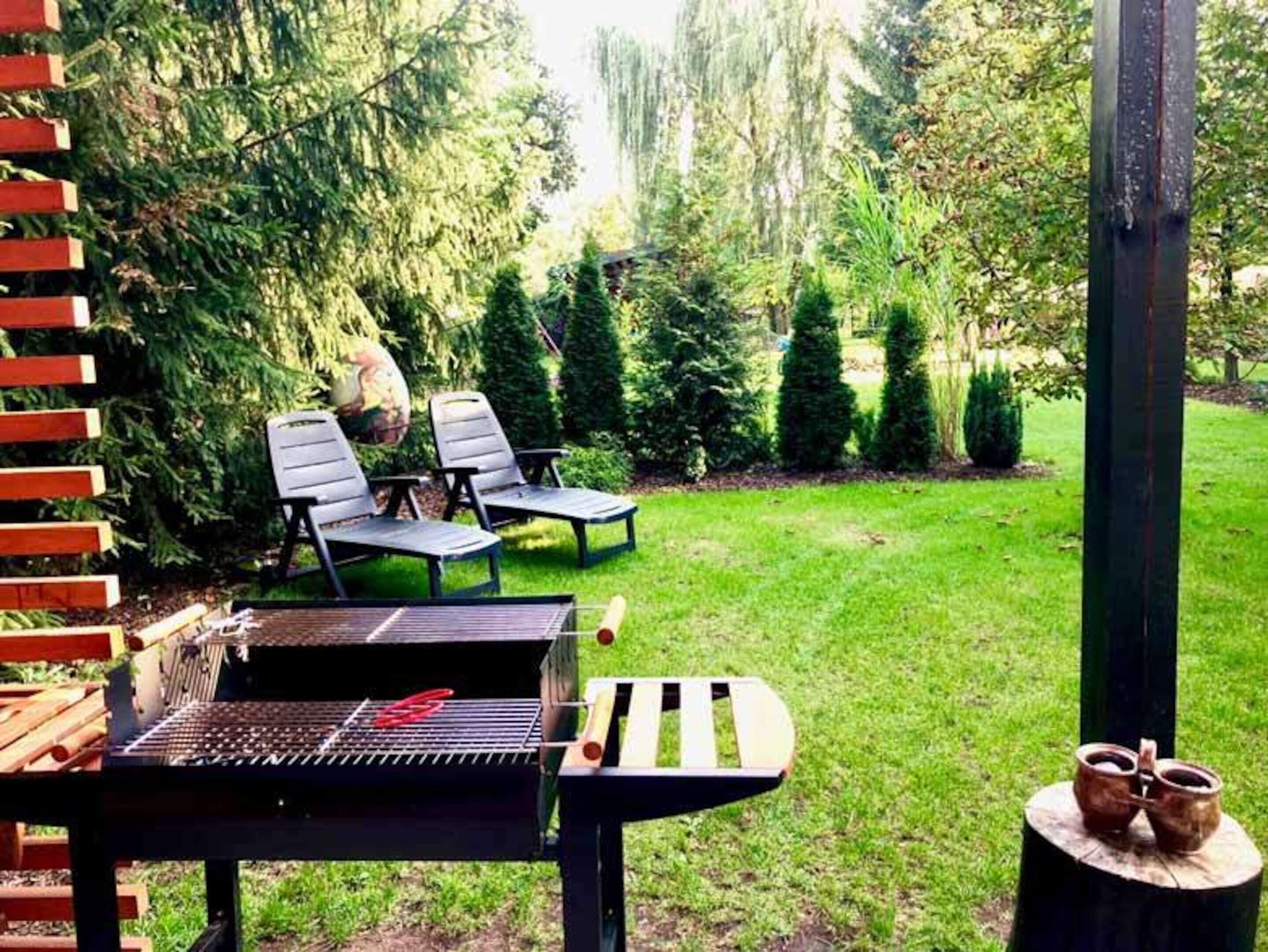 Un patio trasero con una parrilla, dos sillas de jardín y una mesa de madera.