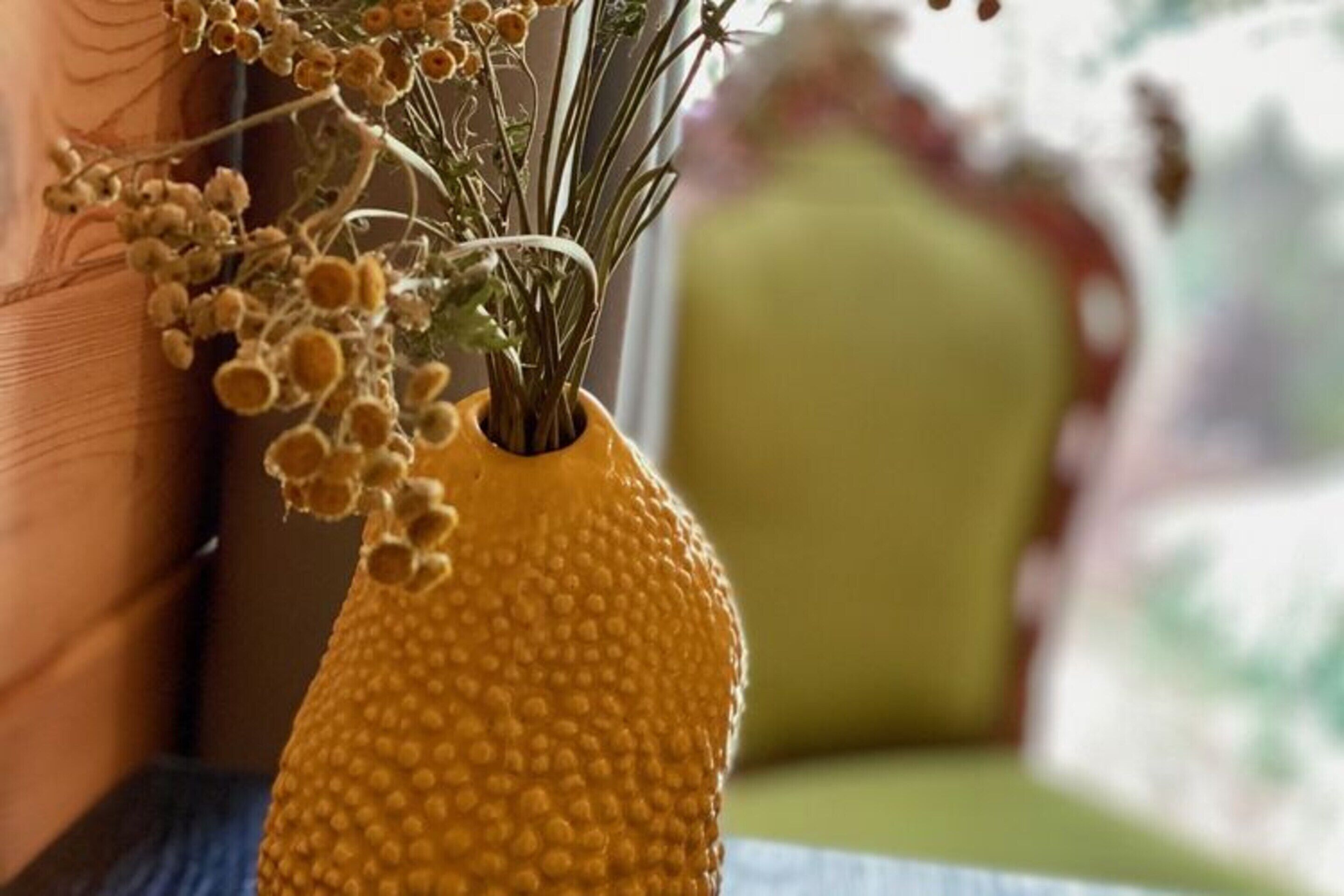A textured yellow vase with dried flowers on a table.