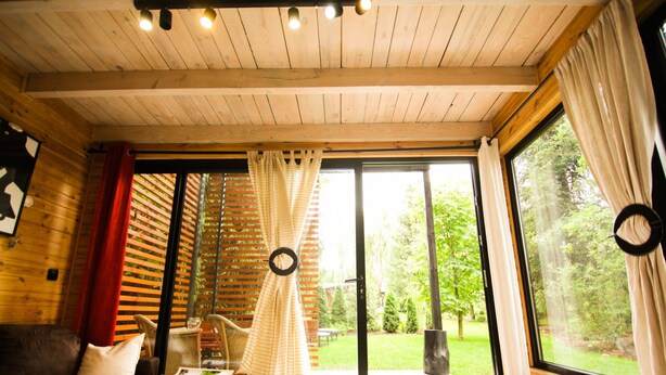 Una habitación acogedora con techo de madera, un sofá, una mesa y un amplio ventanal corredera que da a un espacio exterior.