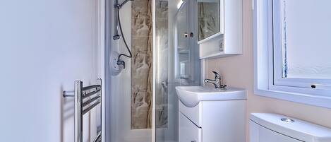 Un baño moderno con ducha de vidrio, un lavamanos blanco y un inodoro.