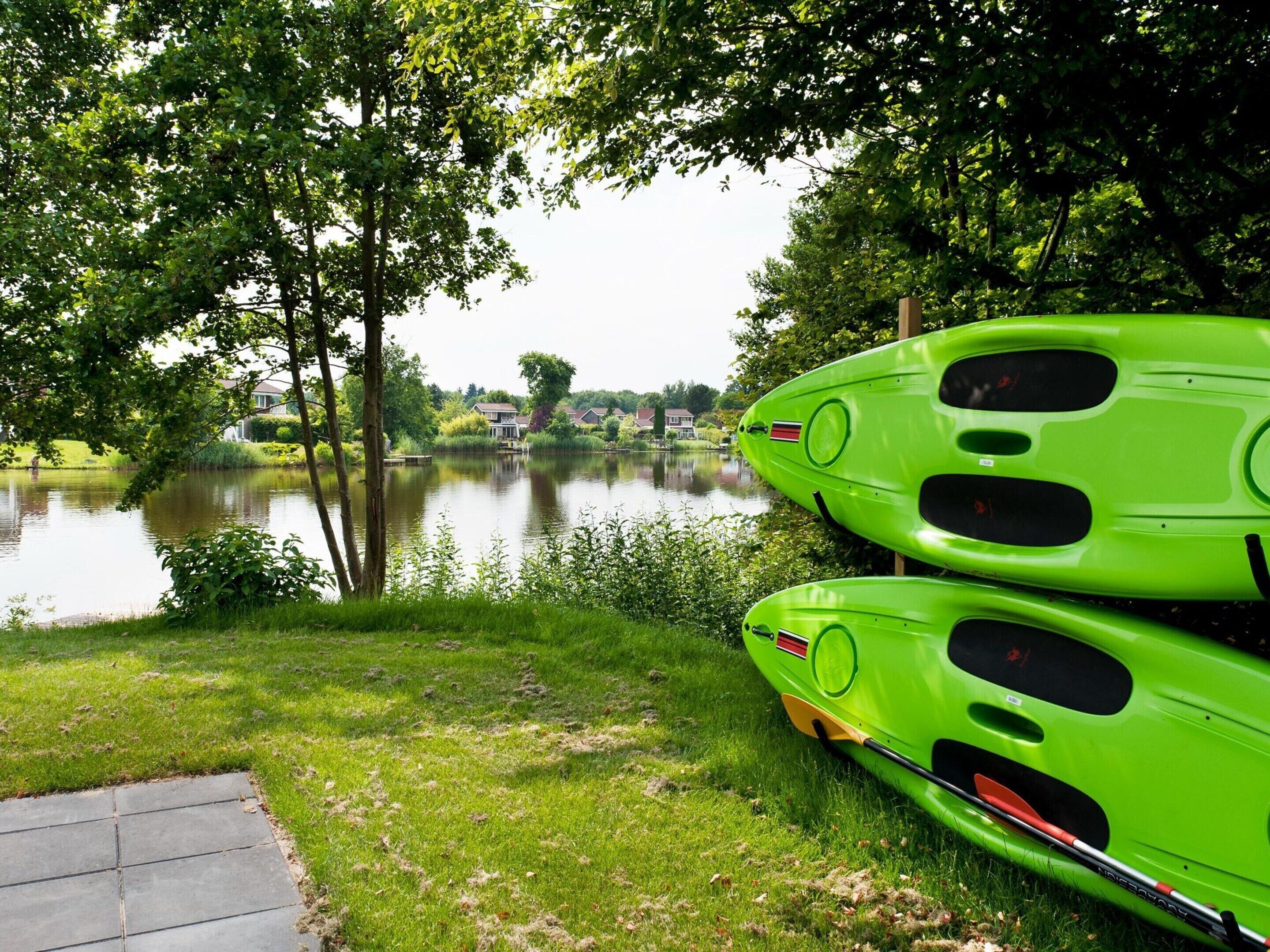 A serene lakeside setting with two bright green kayaks parked on a grassy area.