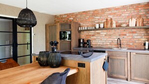 A kitchen with a brick wall, wooden cabinets, and a black hanging light fixture. - Luxury Holiday Home With Sauna in Vlagtwedde (Vlagtwedde)