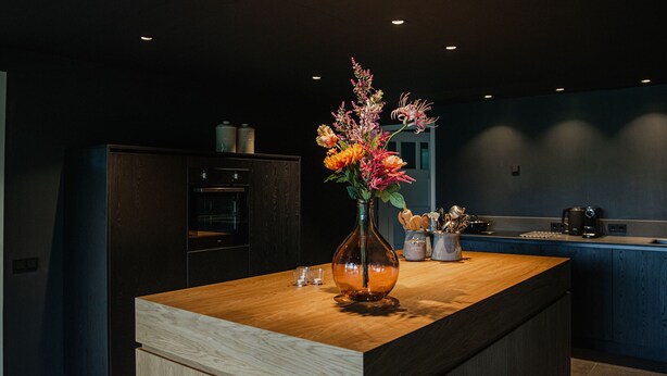 A modern kitchen with a wooden island, dark cabinetry, and a vase of flowers. - House in Leenderstrijp Near Leenderbos Trails (Leende)