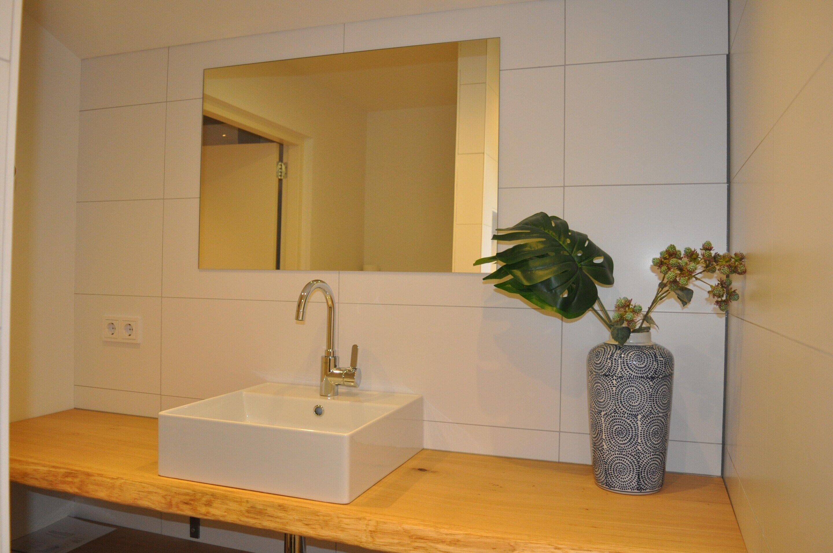 Ein Badezimmer mit einem weißen Waschbecken, einem Spiegel und einer Pflanze in einer Vase.