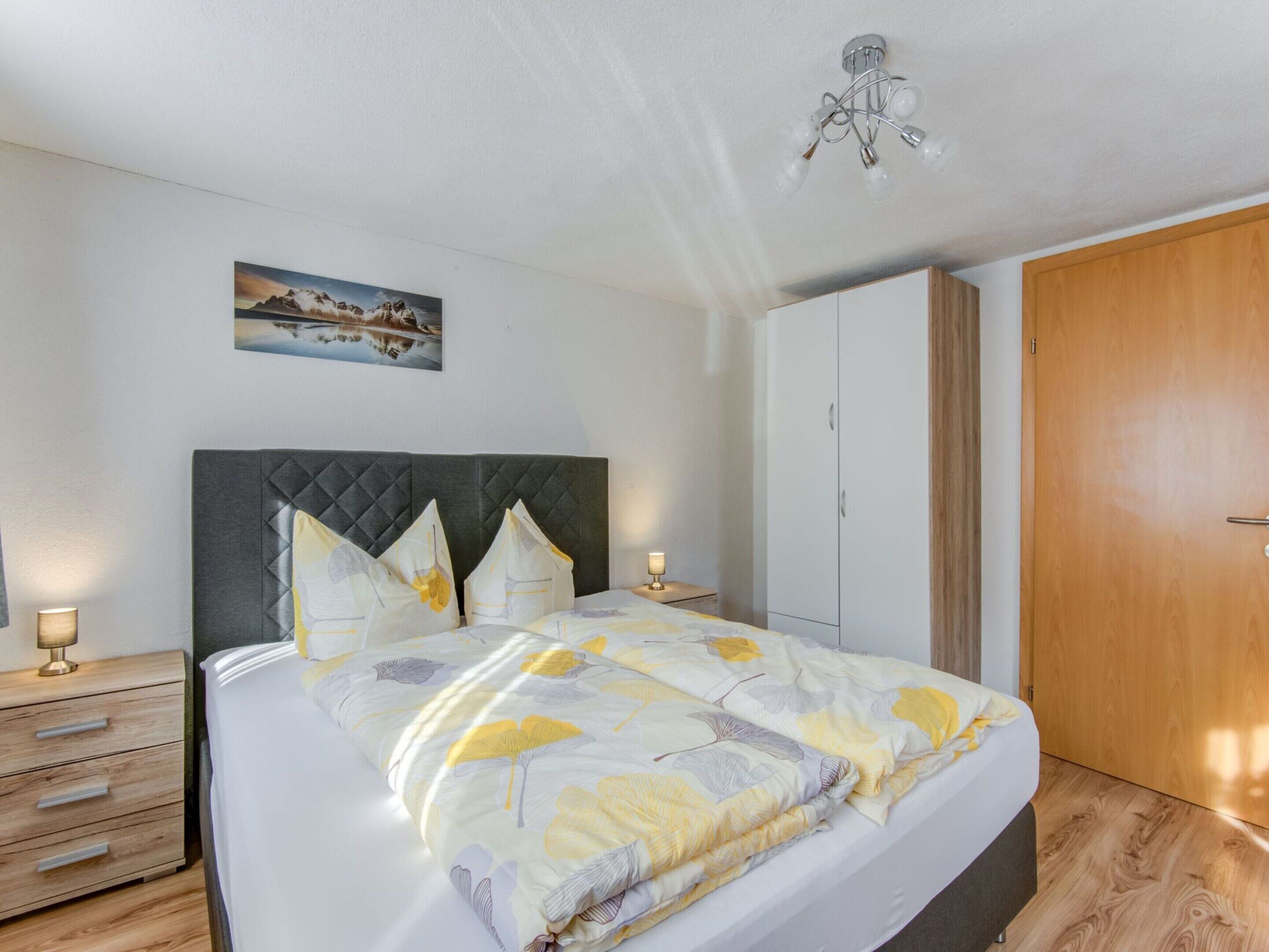 A neatly arranged bedroom with a bed, bedside tables, a wardrobe, and a painting on the wall.