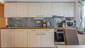 Una cucina compatta con mobili in legno chiaro, schienale piastrellato, microonde, macchina del caffè e lavastoviglie.