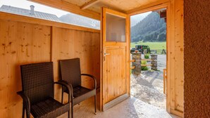 Una baita di legno con due sedie in vimini e un'apertura che dà su uno spazio esterno con un veicolo e un muro di pietra.