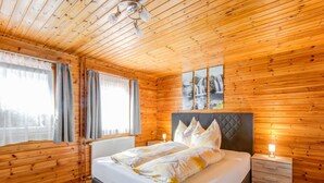 Una camera da letto in una casetta di legno, con un letto, comodini e una finestra con tende.
