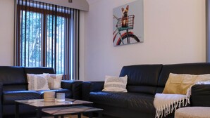A modern living room with a dark leather sofa, a glass coffee table, and a painting of a dog in a basket on the wall. - Retreat Near Maasmechelen (Lanaken)