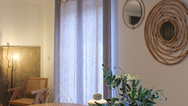 A room with a wooden chair, a table, a plant, a curtain, and a wall-mounted mirror. - Retreat Near Maasmechelen (Lanaken)