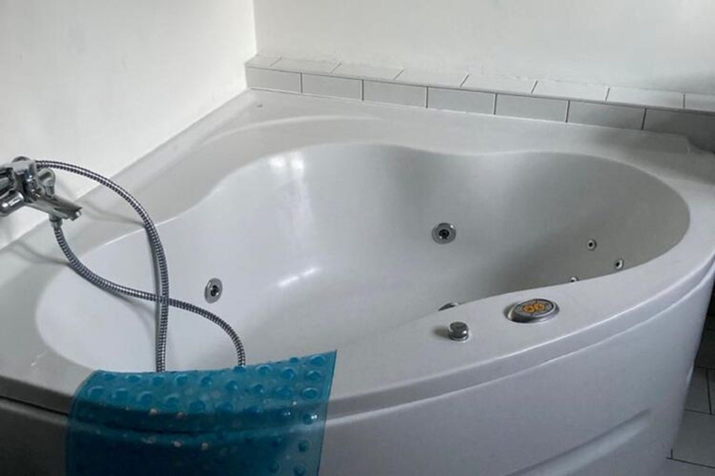 Eine weiße Badewanne mit Duschbrause und blauem Badteppich.