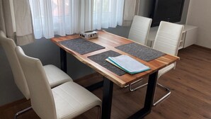 A modern dining area with a wooden table, four white chairs, and a TV on the wall. - Apartment in Mauerbach Near Vienna With Pool (Mauerbach)