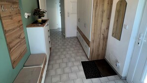Um corredor estreito com um painel de madeira decorativo, um vaso de planta e uma porta que dá para um quarto.