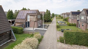 A residential area with modern houses featuring solar panels, a paved driveway, and well-maintained gardens. - Grou Getaway With Bikes & Whirlpool (Grou)