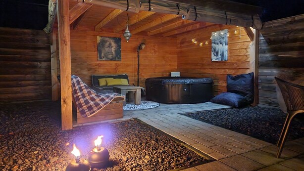 A cozy wooden cabin with a sofa, a massage table, and a small table. There are two candles on the ground. - Grou Getaway With Bikes & Whirlpool (Grou)