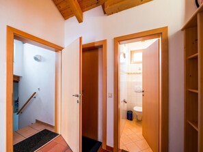Staircase and bathroom access via three doors in a hallway with a tiled floor and wooden ceiling.