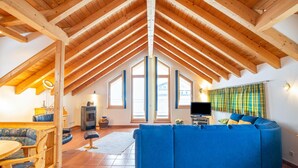 A spacious loft with a high ceiling, wooden beams, a blue sofa, a dining area, and large windows. - Penthouse Apartment in Wagrain Near ski Area (Wagrain)