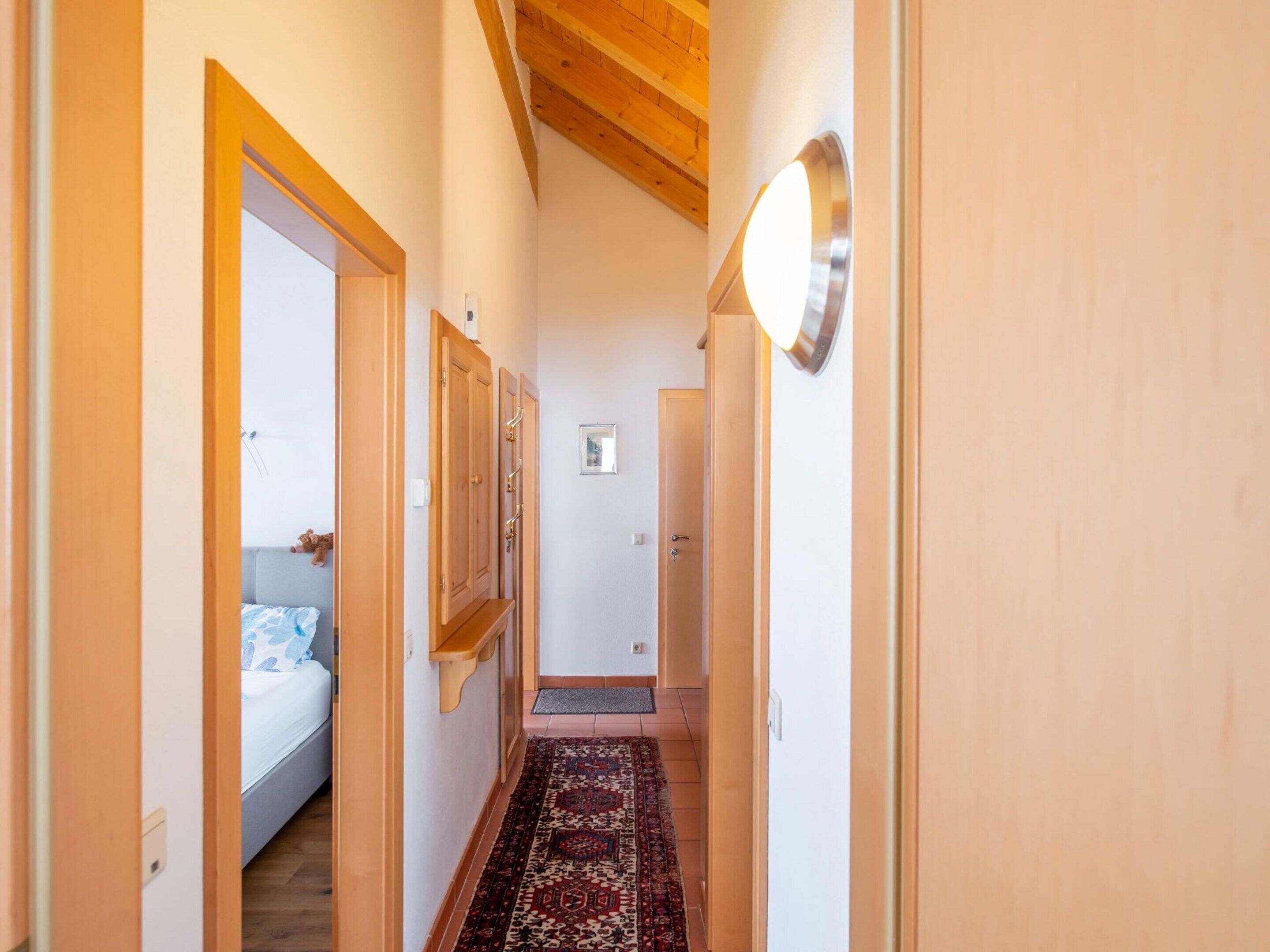 Un corridoio stretto con porte in legno, un tappeto decorato e un soffitto con travi a vista.