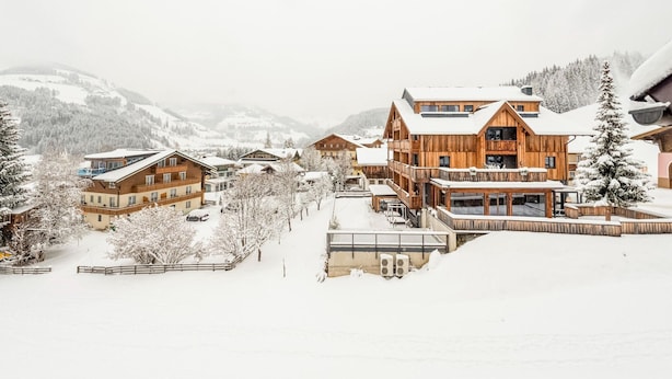 A snow-covered village with wooden buildings, including a large lodge with balconies and a ski lift visible in the background. - Penthouse Apartment in Wagrain Near ski Area (Wagrain)