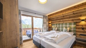 Cama doble con cabecera de cuadros, piso de madera y balcón con vistas a la montaña.