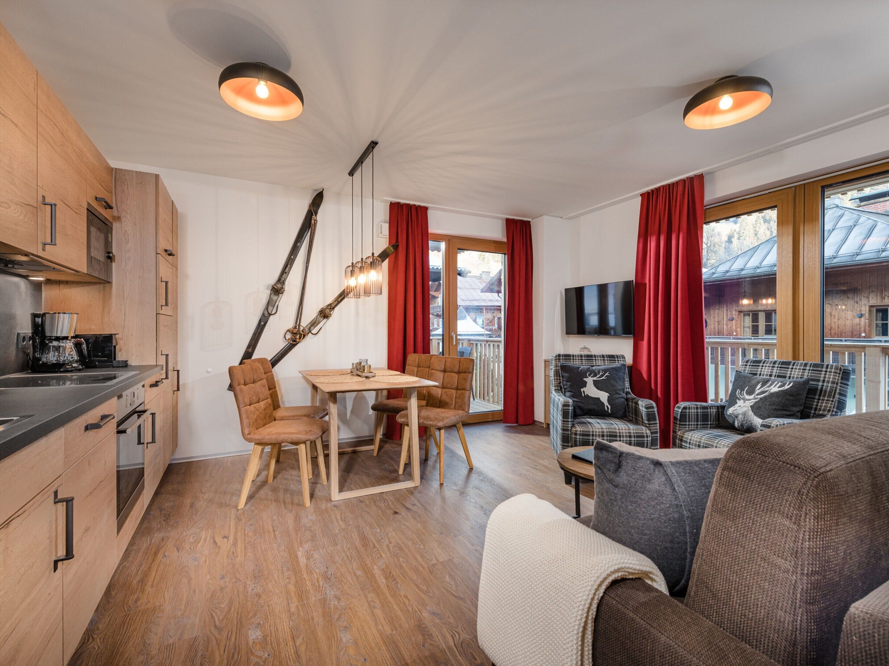 Eine moderne Küche mit Holzausstattung und einem Essbereich mit Tisch und Stühlen. Im Wohnbereich befindet sich eine Couch und ein Fernseher.