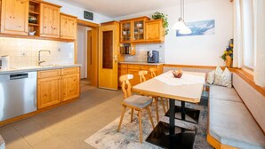 A modern kitchen with wooden cabinets, a dining area with a table and chairs, and a built-in bench. - Apartment in Kappl Right by the ski Lift (Kappl)