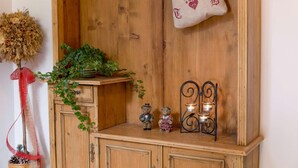 Un mueble de madera con un pequeño estante, un lazo rojo, un arreglo de flores secas, una planta en maceta, dos osos de peluche y un candelabro.