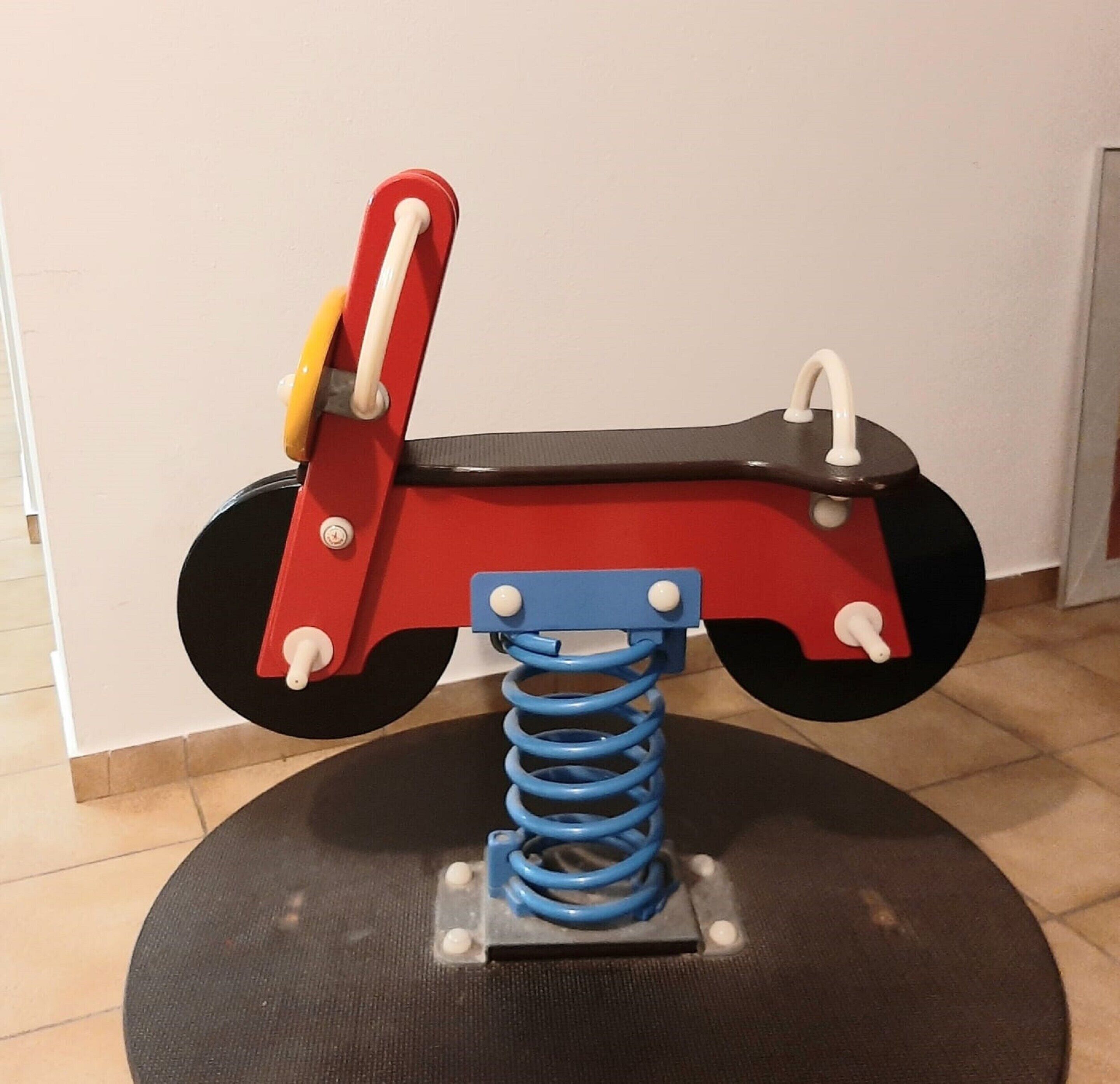 A red and black toy car with a blue spring base on a round mat.