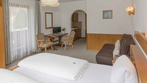 Habitación de hotel con una cama grande, un escritorio con dos sillas, una kitchenette pequeña y un sofá.