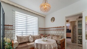 A cozy living room with a sofa, a round table with a lace tablecloth, a decorative chandelier, and patterned wall tiles. - Vlissingen Home Near the Beach (Vlissingen)