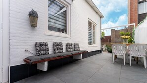 A patio with a bench, white chairs, and a table. - Vlissingen Home Near the Beach (Vlissingen)