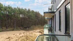 A modern building with a glass balcony overlooking a forested area.