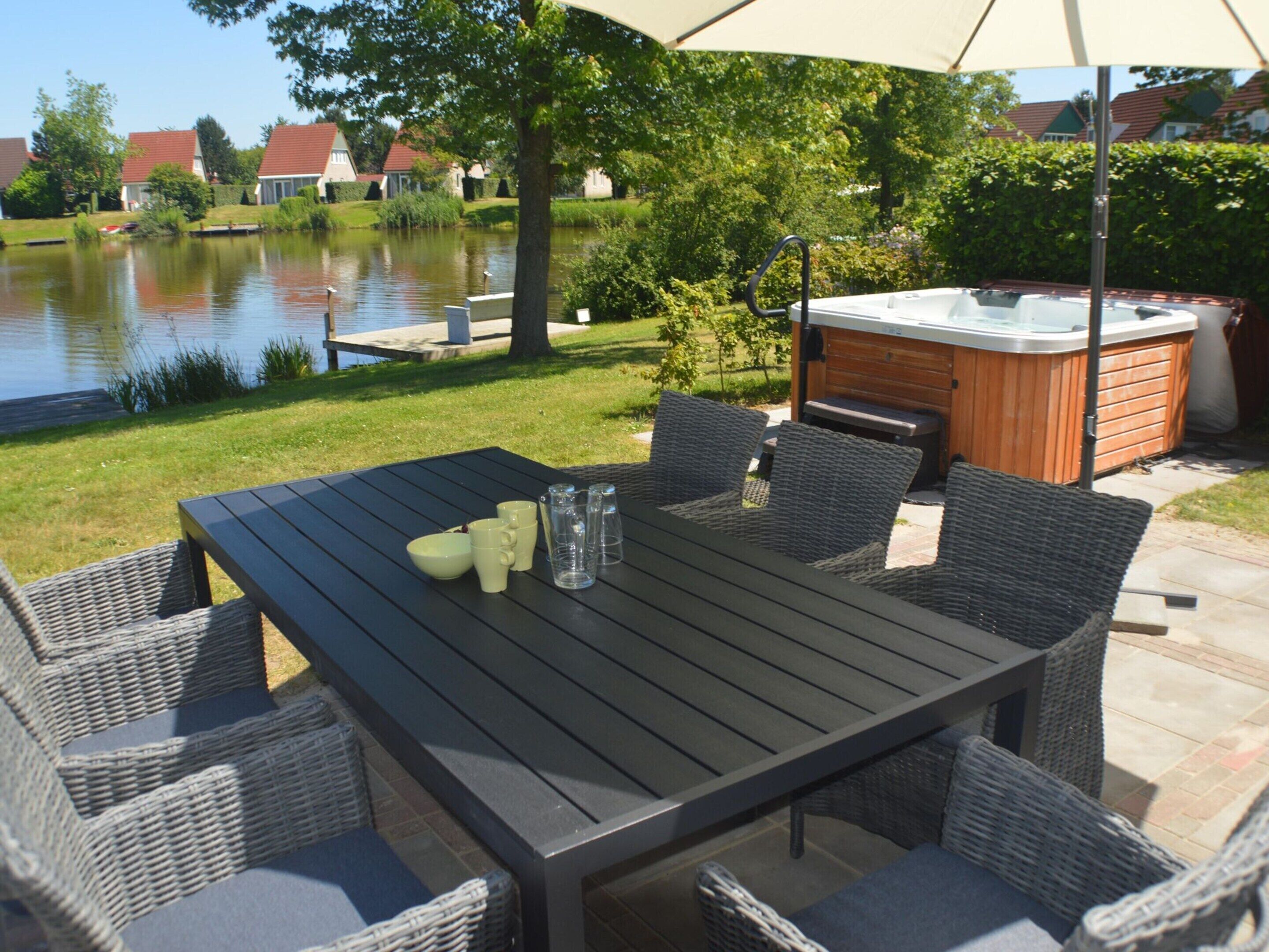 Une terrasse extérieure avec une table et des chaises, un jacuzzi et une vue sur un lac.