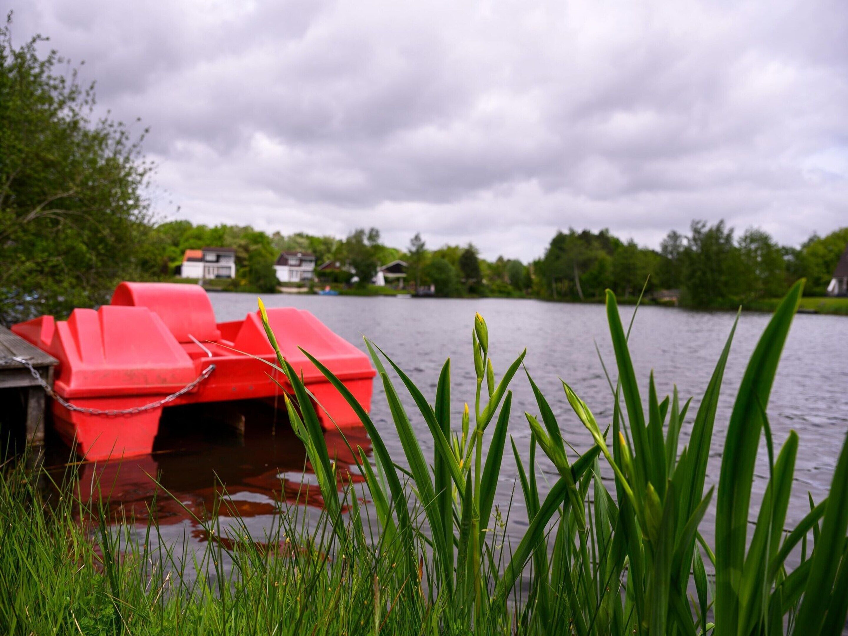 A red boat docked at a lakeside pier with houses in the background.