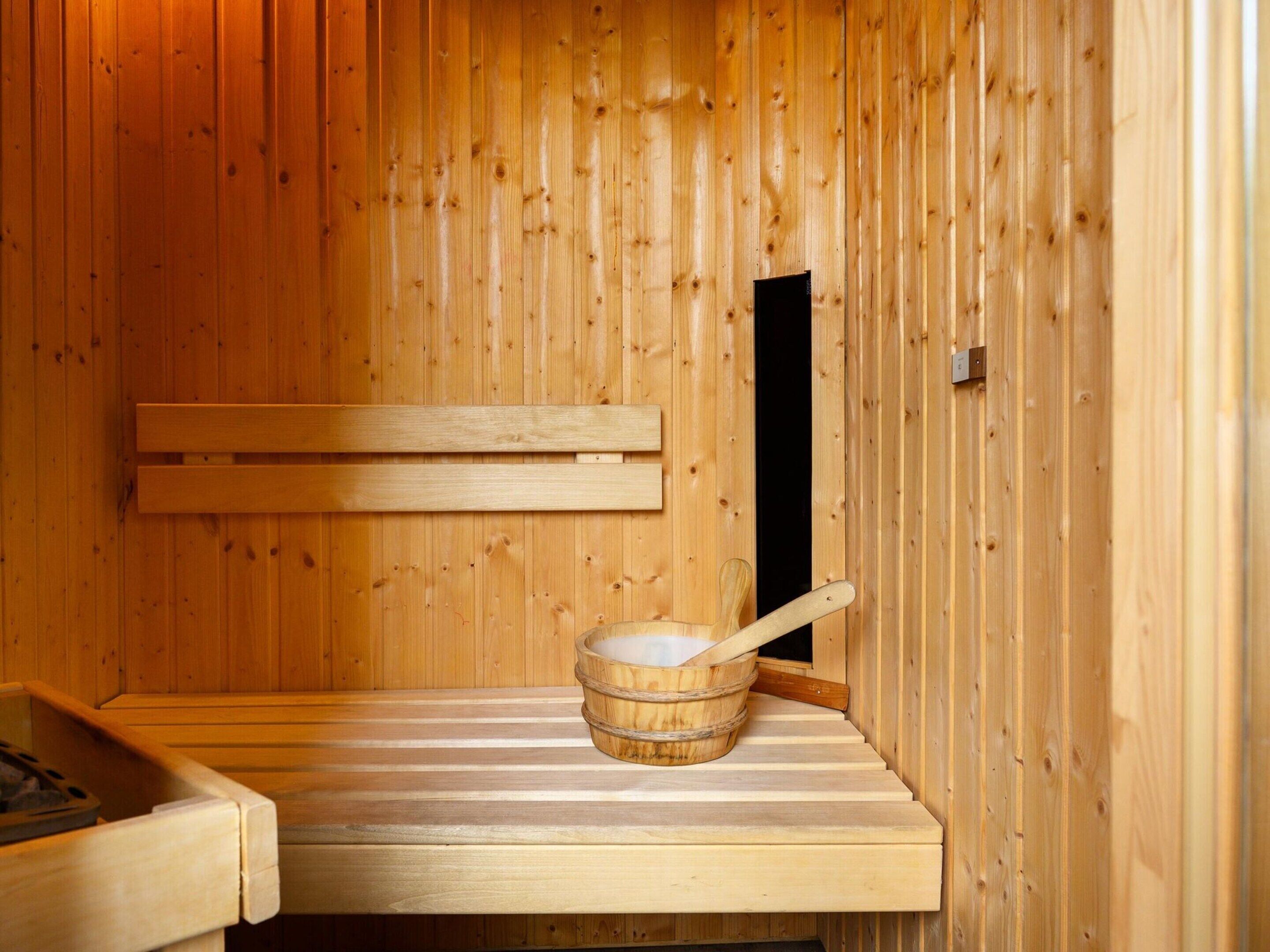 A wooden sauna with a bench, a wooden bucket with a scoop, and a small window.