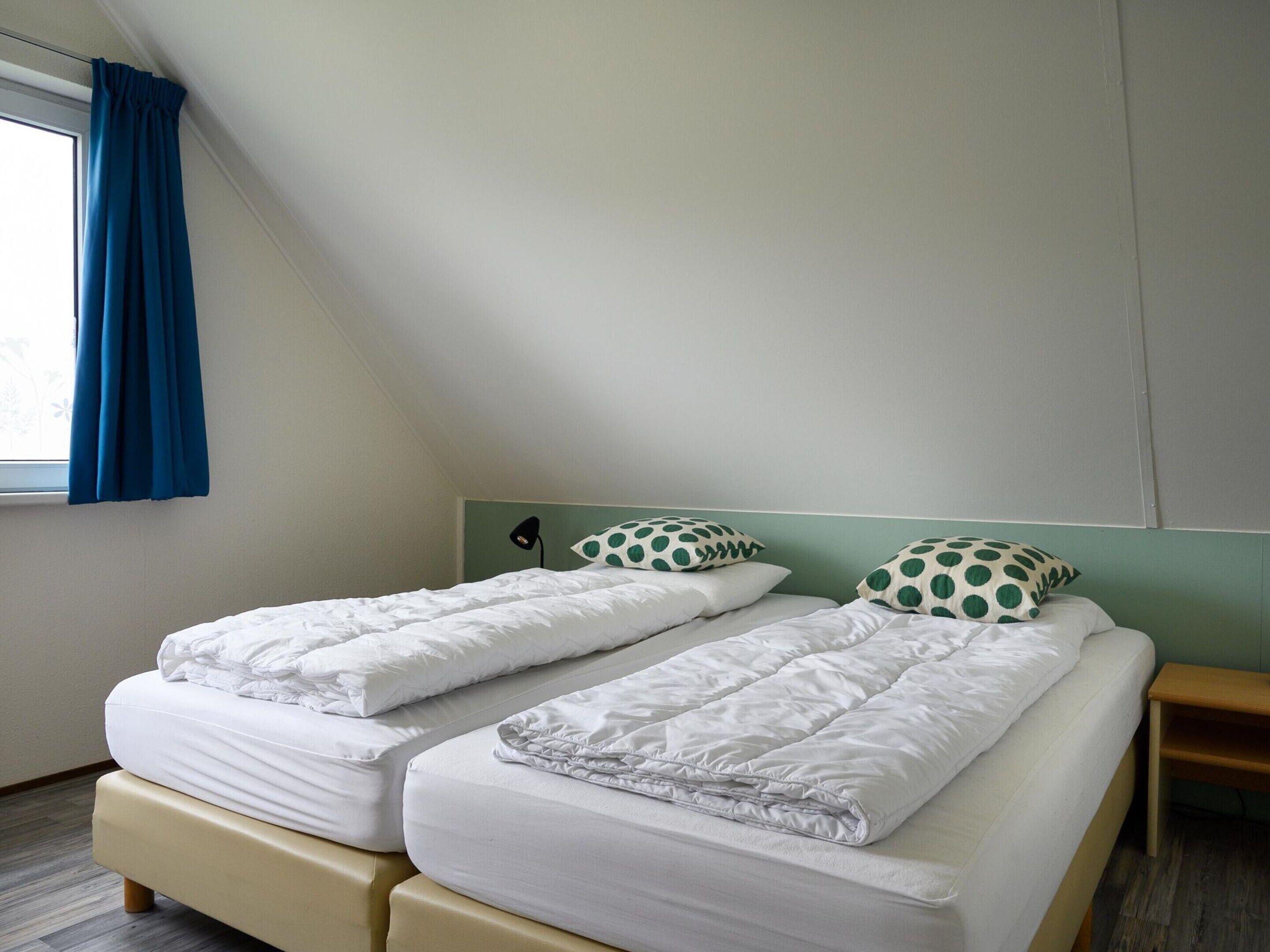 A twin room with two beds, a window with blue curtains, and a green wall.