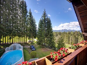 A wooden deck with flower planters, a swimming pool, and a view of a forest and mountains. - Apartment in Mooswald in Carinthia With Pool (Fresach)