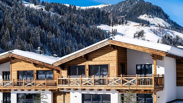 Una cabaña de madera con balcón, con una imponente montaña nevada al fondo.