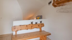 A wooden bench in a room with white walls, a sloped ceiling, and a small shelf with decorative items. - Fantastic Holiday Home Near Zell am See, Kaprun (Piesendorf)
