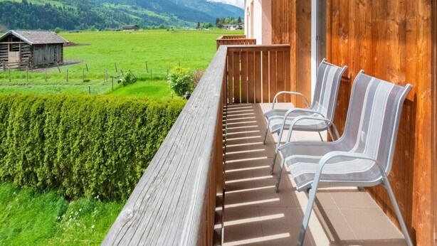 A wooden balcony with two chairs and a view of a green field and mountains. - Fantastic Holiday Home Near Zell am See, Kaprun (Piesendorf)